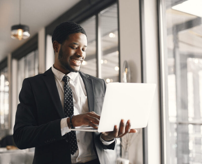 African man in a black suit. Guy with beard. Man with laptop.