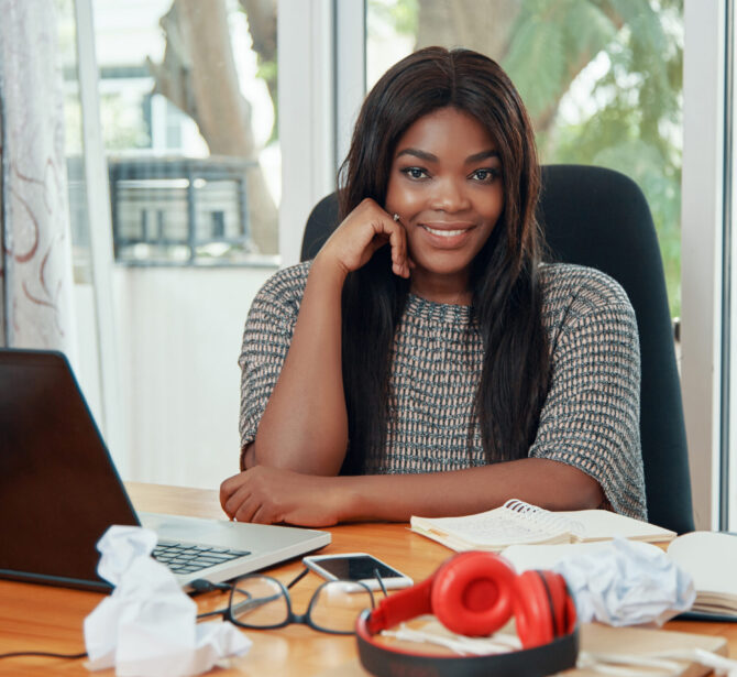 Charming stylish African American woman sitting at table in office smiling at camera